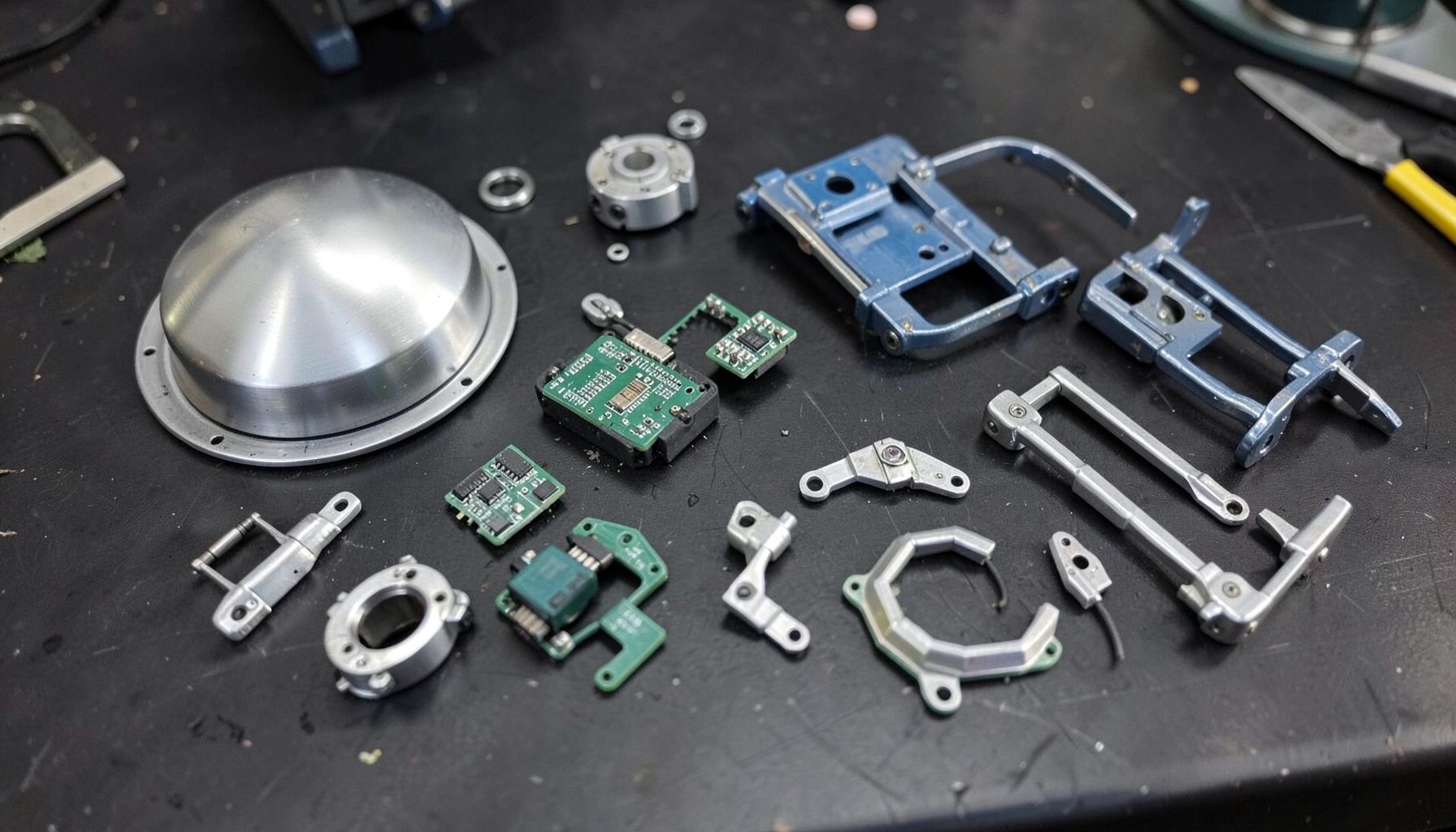 Assorted astromech droid components laid out on a dark workbench — aluminum dome, circuit boards, motor controllers, and wiring